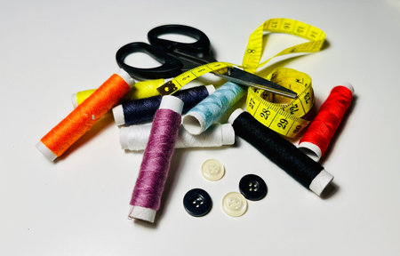 spools of thread, scissors, buttons and measuring tape on white background