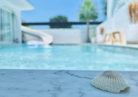 Seashell on white marble table with swimming pool background, shallow depth of field
