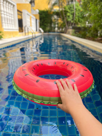 Woman's hand holding inflatable ring in swimming pool on sunny day