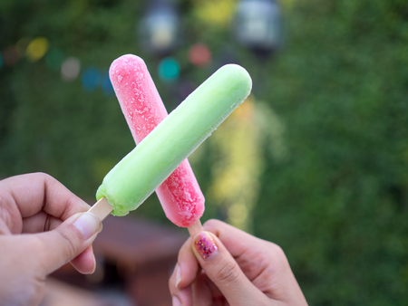 Hand holding green and red ice cream sticks overlapping green backgroundの写真素材