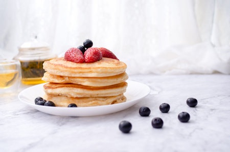 Stack of pancakes with topping, strawberry and blueberry.Placed in a white plate on a marble table...
