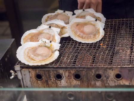 Many large scallops roast on the stove to sale for customer at Kuromon market.Scallops are a popular...