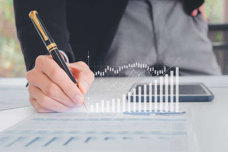 Close up hand businessman writing with pen, financial data and sales rates and market exchanges or appropriate paper reports with graphs showing business growth. Concepts of financial investmentの写真素材