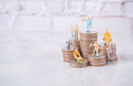 Selective focus engineering people and architecture miniature workers team working standing on stack of coin, with blue background.Team work financial business and construction success concept.の写真素材