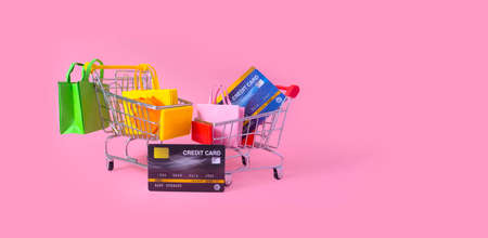 Multi-colored paper shopping bag and credit card in cart on pink background.Buying concept. Online shopping and store and business discounts.の写真素材