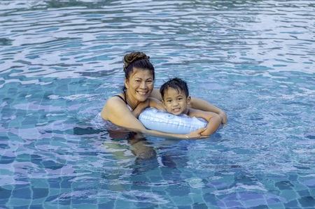 Beautiful mother teaching cute baby girl how to swim in a swimming pool. Child having fun in water with mom.の写真素材