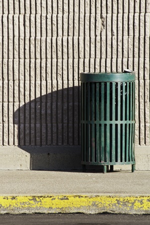 A green trash can in a public area near a brick wall on a sidewalk with a curb. の写真素材