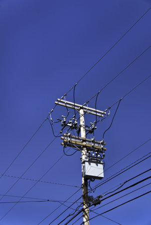 A telephone pole and wires or cables against a bright blue sky. 