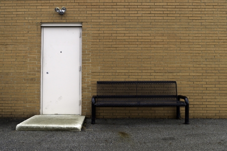 A bench and a door against a light colored brick wall. の写真素材
