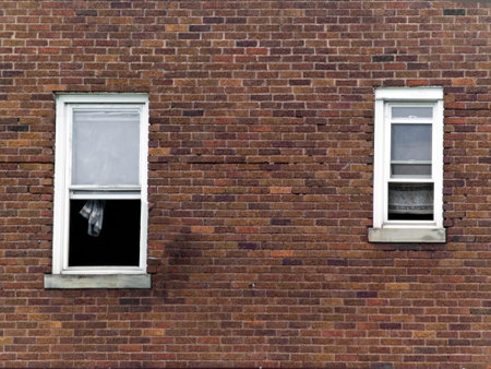 Red brick wall with open windows and curtains. 