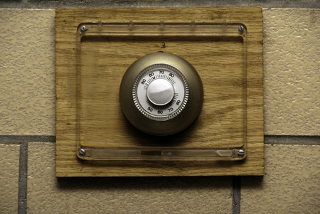 A thermostat mounted on a wooden board mounted on a block wall.の写真素材