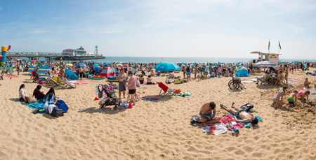 Bournemouth, UK - August 28, 2017:Busy beach in a hot summer day with Pier Amusements in the backgroundのeditorial素材