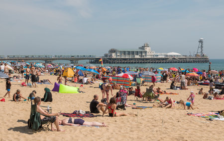 Bournemouth, UK - August 28, 2017:Busy beach in a hot summer day with Pier Amusements in the backgroundのeditorial素材