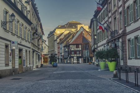 A typical Alsatian street with half-timbered houses. On Sunday morning, there are no residents or tourists on the street. On the day of the parliamentary elections, the three-color national flags of France are hanging on the official buildingのeditorial素材
