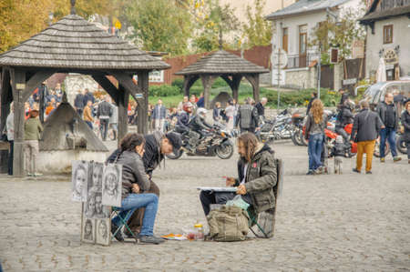 the market square in Kazimierz Dolny, couple of tourists poses for a portrait for a painter, attractions of a tourist town, historic old wells covered with a wooden roofのeditorial素材