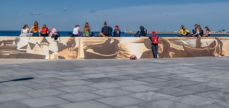 Hel, pomorskie/Poland-06-09-2019 Last weekend before summer the youth rests on the seafront on a coastal wall covered with paintings from the life of fishermen on the square by the wall of tire tracksのeditorial素材