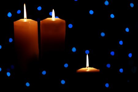 Three burning candles with blue lights in background, dark shadowsの写真素材