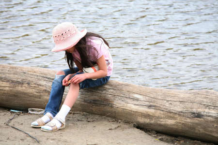 Girl with wound sitting on log by riverの写真素材