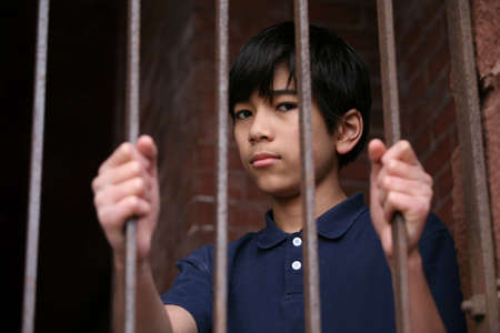 Boy standing behind bars, sad  or wary expressionの写真素材