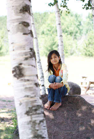 beautiful little girl quietly sitting under treesの写真素材