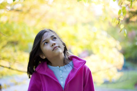 young girl looking up at autumn leavesの写真素材