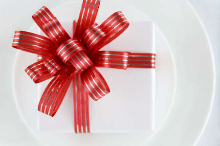 White present with red ribbons on a dinner plate, christmas themeの写真素材