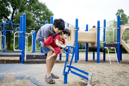 Older brother helping disabled sibling play at playgroundの写真素材