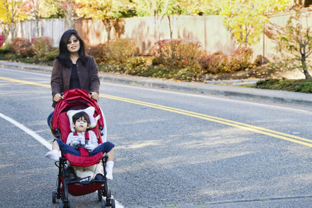 Mother walking with her disabled son in stroller outdoorsの写真素材