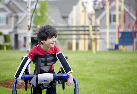 Disabled four year old boy standing in walker near a playgroundの写真素材
