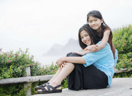 Two beautiful sisters sitting together near a misty ocean in the backgroundの写真素材