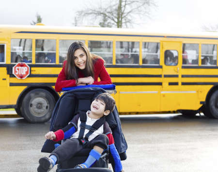 Big sister with disabled brother in wheelchair by school busの写真素材