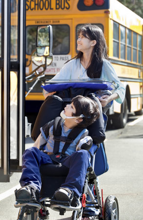 Ten year old girl  pushing disabled little boy wearing protective gear  in wheelchair  next to...