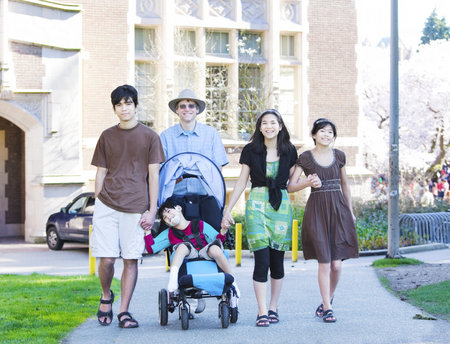 Father walking with his biracial children outdoors. Disabled son in wheelchair has cerebral palsy.の写真素材