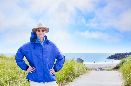 Handsome caucasian man in forties wearing rain jacket by ocean shoreの写真素材