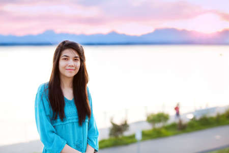 Beautiful biracial young teen girl enjoying outdoors by lake at sunsetの写真素材