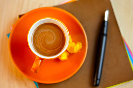 Orange cup of coffee on brown writing paper with pen. View from aboveの写真素材