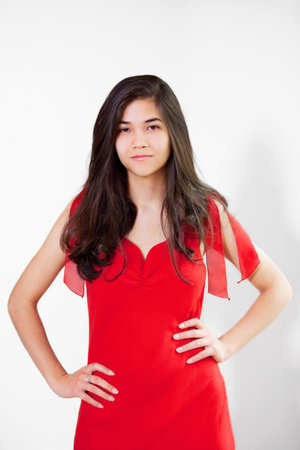 Beautiful biracial teen girl in elegant red dress, hands on hips, relaxedの写真素材