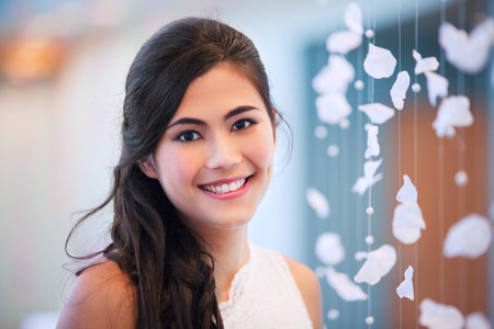 Beautiful biracial bride smiling next to curtain of white rose petalsの写真素材