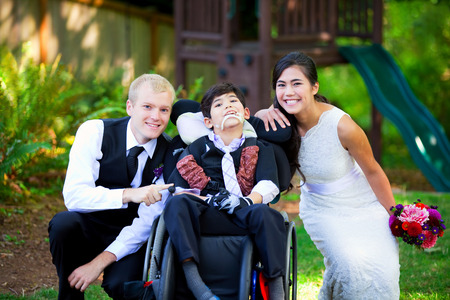 Biracial bride and groom with her little disabled brother in wheelchair on their wedding dayの写真素材