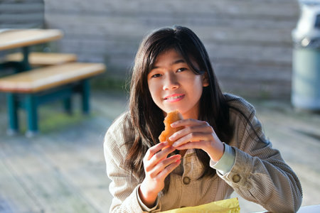 Young biracial teen girl outdoors eating hamburgerの写真素材