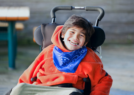 Handsome, happy biracial eight year old boy smiling in wheelchair outdoorsの写真素材