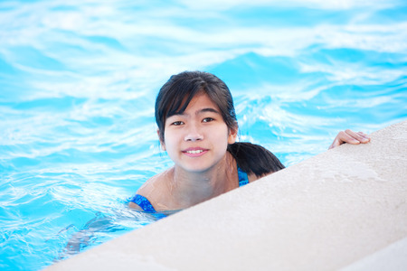 Young biracial Asian teen girl relaxing in pool, smiling at cameraの写真素材