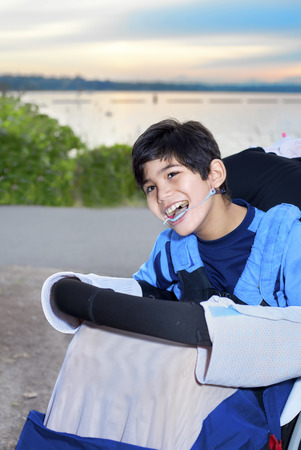 Happy disabled boy sitting  in wheelchair by lake at duskの写真素材