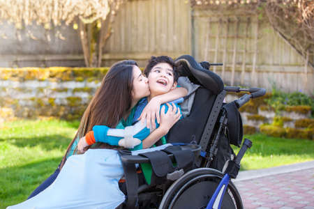 Sister kissing and hugging disabled little nine year old  brother in wheelchair outdoorsの写真素材