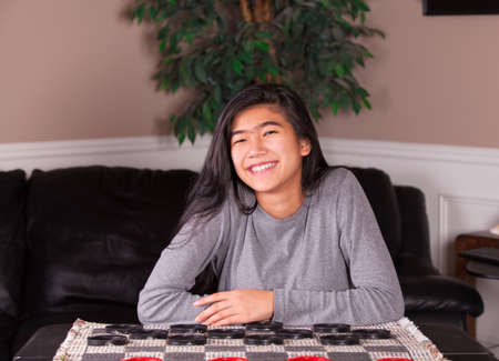 Biracial teen girl sitting at checkers board, ready to play a game with large red and black checker  piecesの写真素材