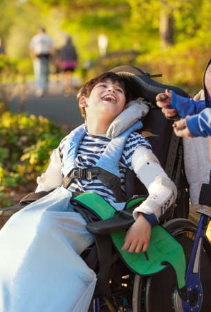 Smiling nine year old boy in wheelchair enjoying time at park outdoorsの写真素材