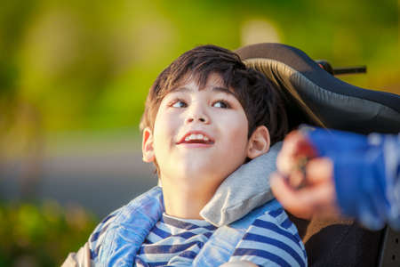 Handsome disabled nine year old boy sitting in wheelchair outdoors looking up into skyの写真素材