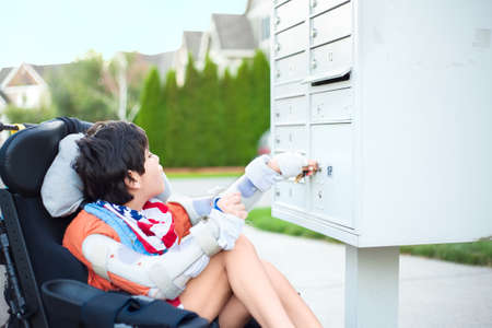 Disabled ten year old boy in wheelchair using key to open mailbox outdoorsの写真素材