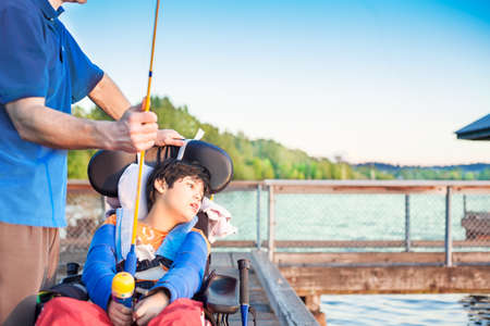 Caucasian father helping disabled ten year old son in wheelchair fish off pierの写真素材