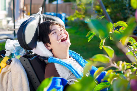 Disabled biracial ten year old boy in wheelchair relaxed and laughing  in back yardの写真素材